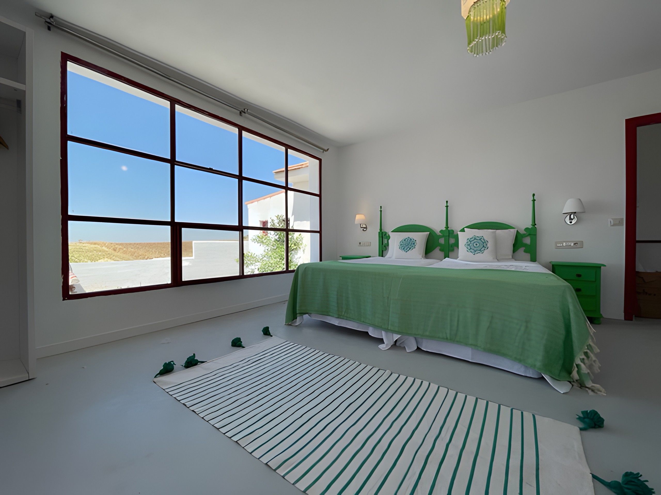 Une chambre avec une grande fenêtre, un lit vert et un tapis à rayures.