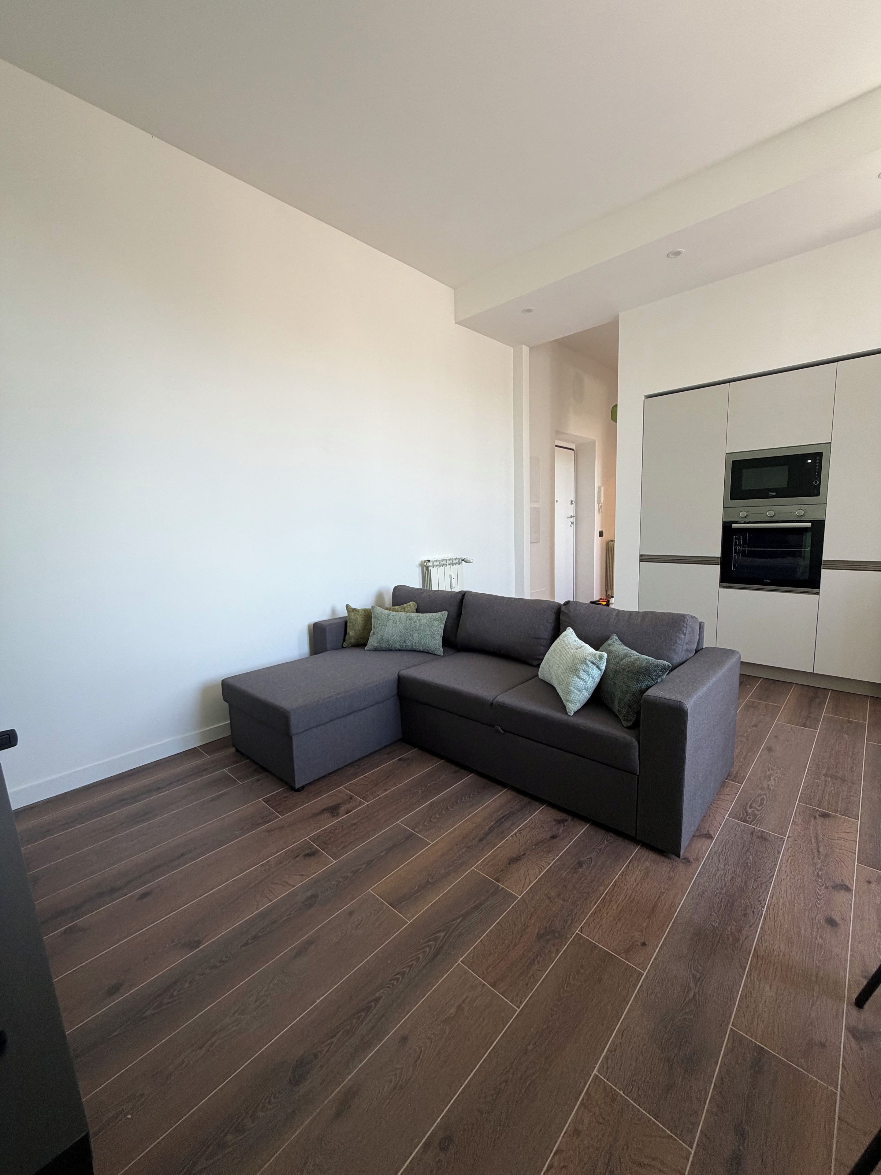 A modern living room with a sectional sofa, a built-in oven, and a wooden floor.