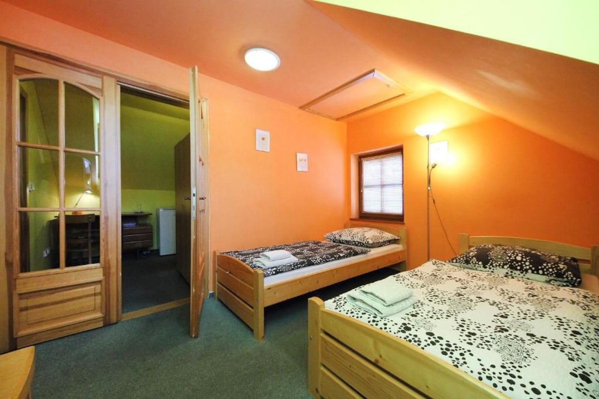 Quarto pequeno com duas camas de solteiro, guarda-roupa de madeira, porta deslizante para o banheiro e luminária fixada na parede.