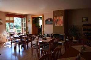Uma sala de jantar com mesas e cadeiras de madeira, lareira e estante de livros.