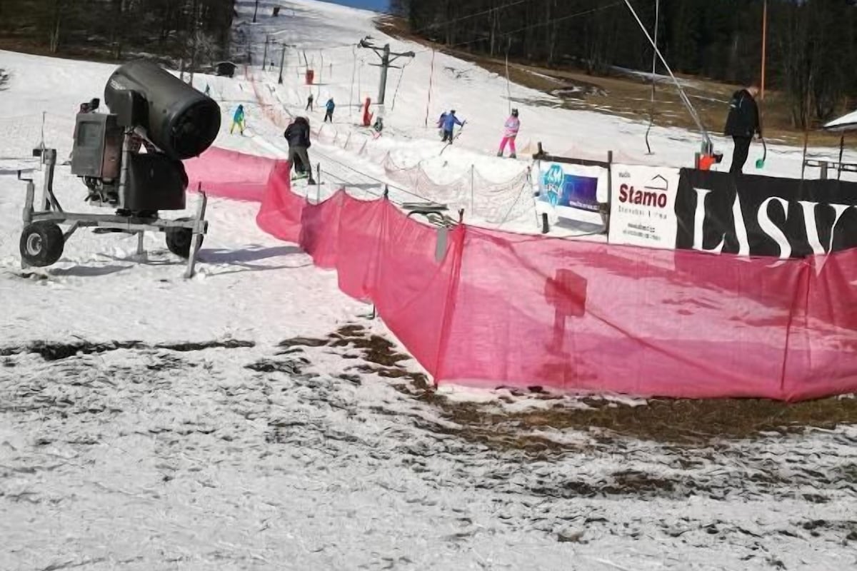 Pista de esqui com teleférico, rede de segurança vermelha e um banner com a palavra 'LASU'.