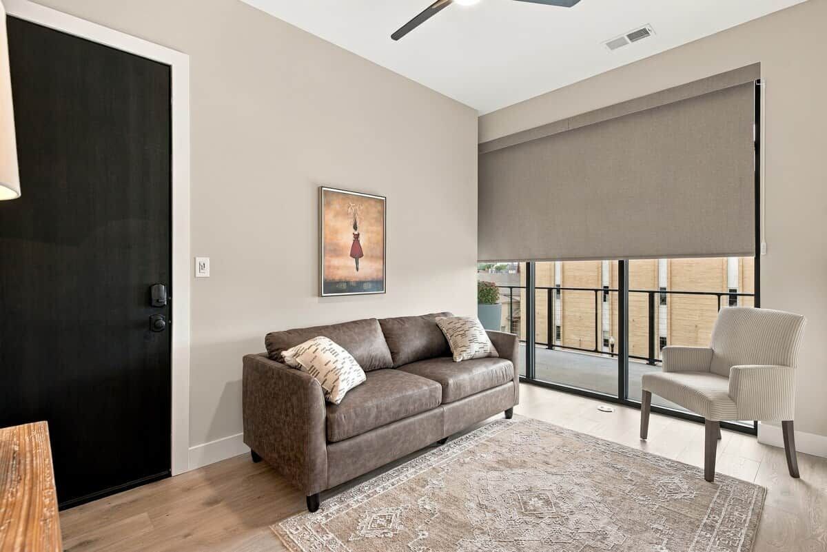 A modern living room with a dark-colored sofa, a patterned rug, and a large window with a view of the outside.