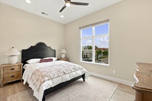 Ein Schlafzimmer mit Bett, Nachttischen, Deckenventilator, Fenster mit Blick und Holzboden.