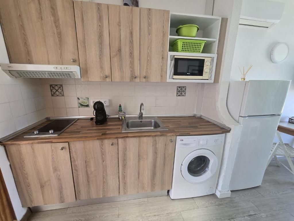 A compact kitchen with wooden cabinets, a built-in microwave, a washing machine, and a sink.