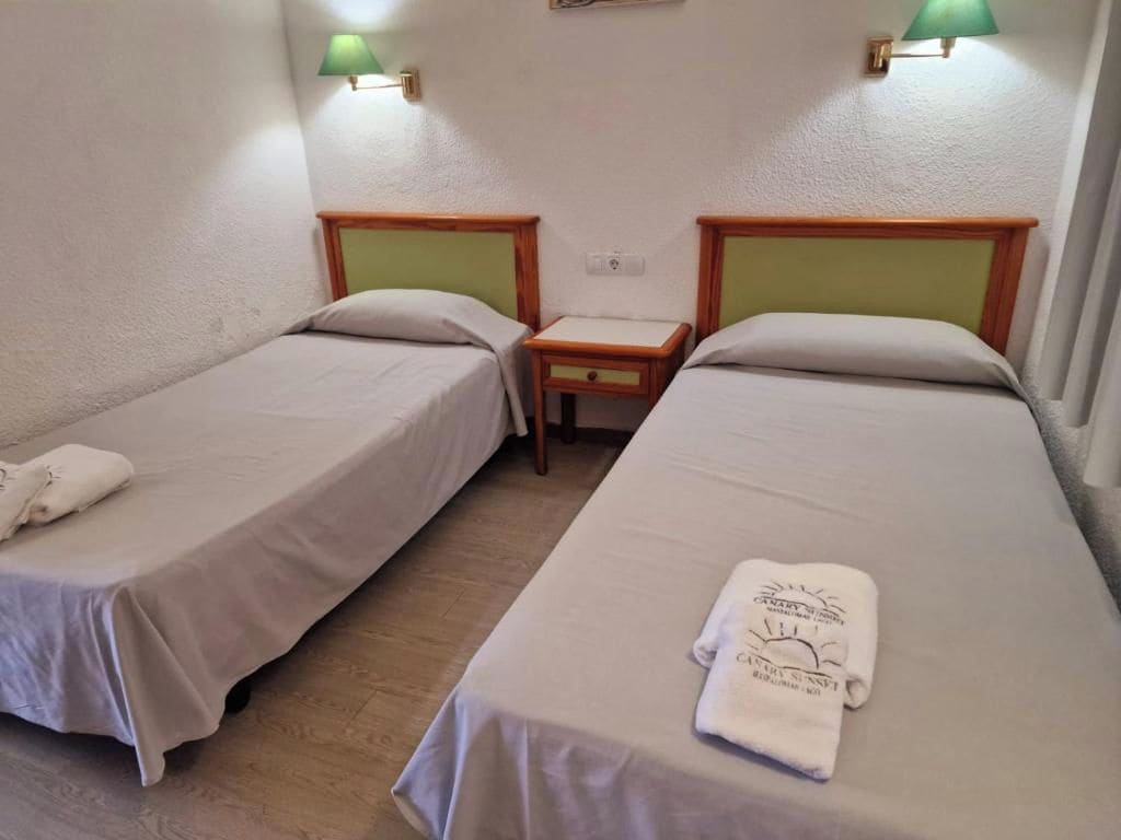 Una habitación con dos camas individuales, una mesita pequeña y dos lámparas de pared.