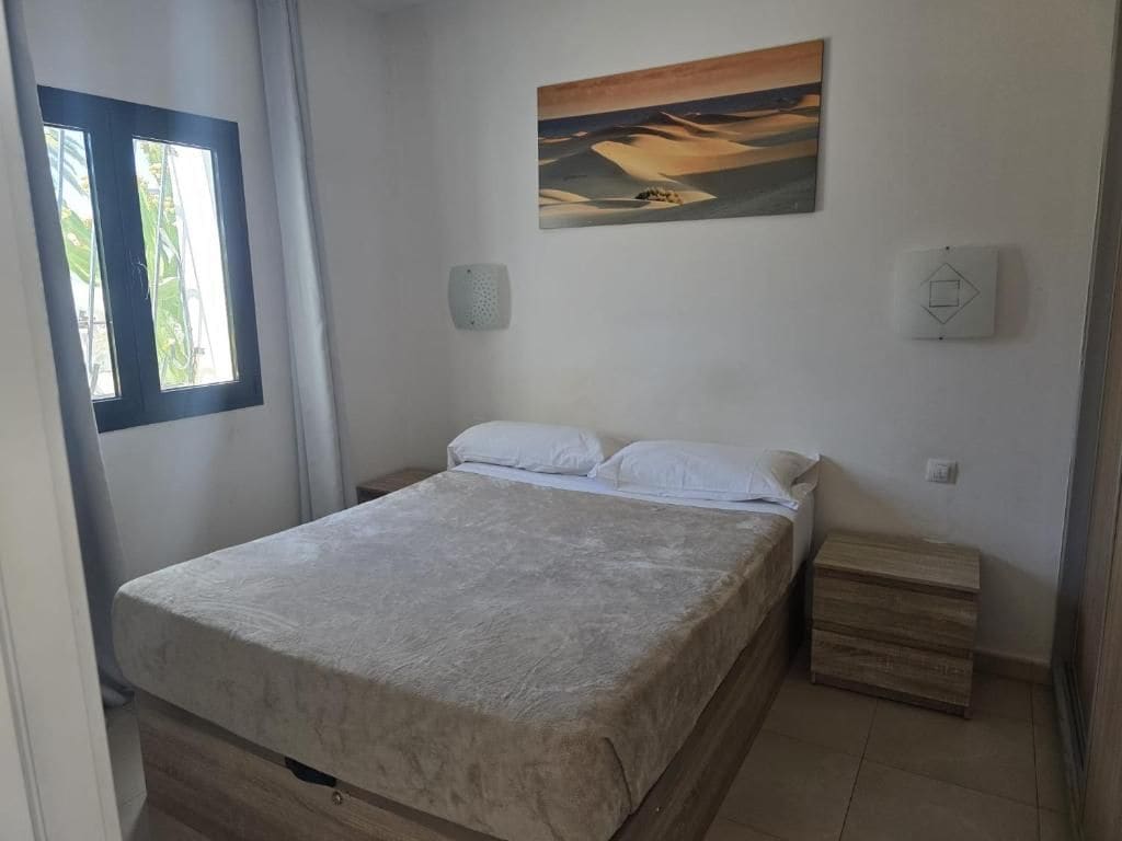 Ein Schlafzimmer mit einem Bett, einem Nachttisch, einer Wandleuchte und einem Gemälde.