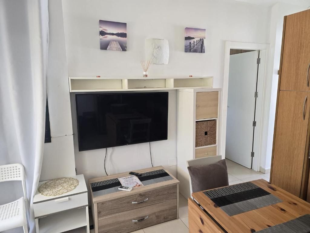 Ein Wohnzimmer mit Flachbildfernseher, Couchtisch aus Holz, weißem Beistelltisch und braunem Sessel.