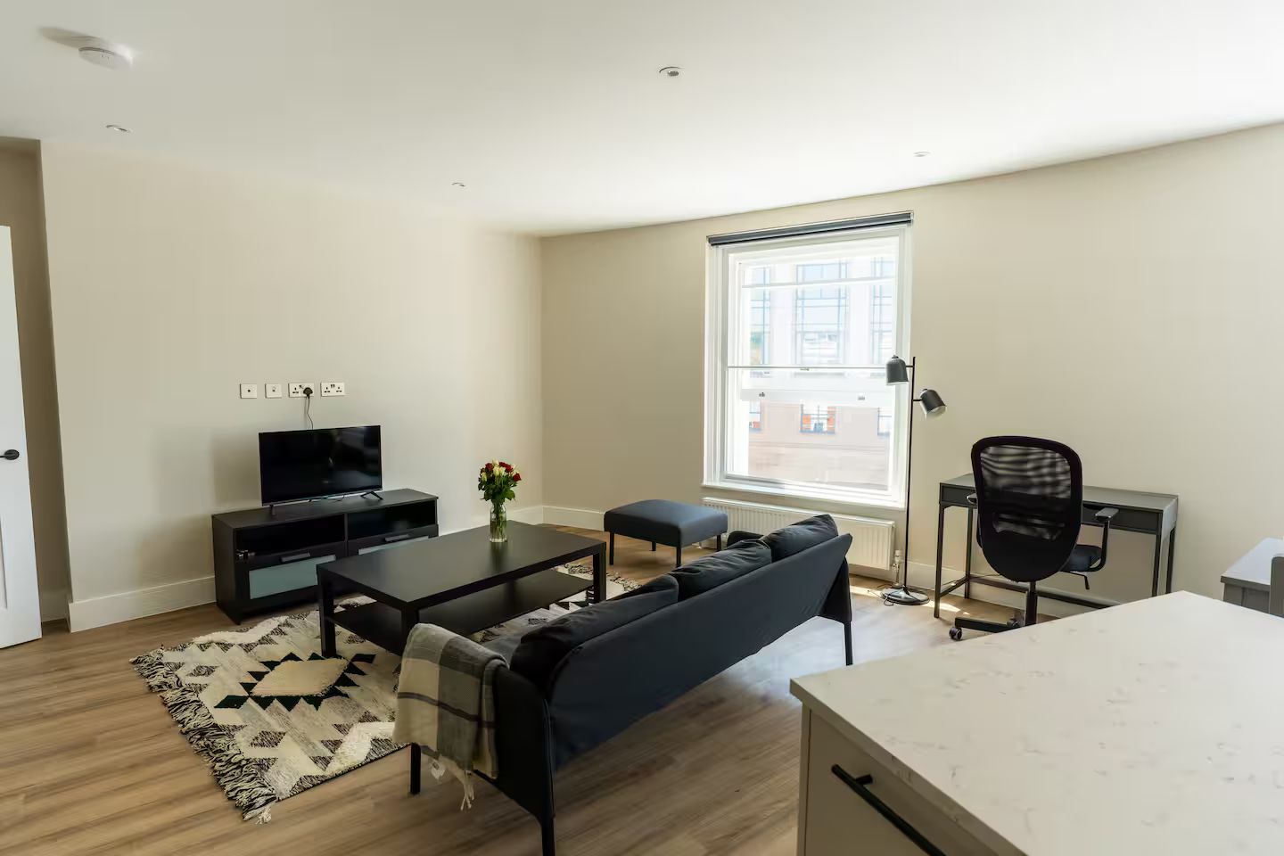 A modern living room with a flat-screen TV, a sofa, a coffee table, and a dining area with a table and chairs.