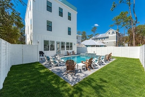Un jardin avec une piscine, des chaises longues et une clôture blanche.