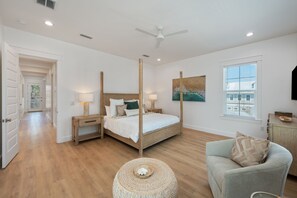 A bedroom with a four-poster bed, bedside tables, a round woven ottoman, a grey armchair, and a painting on the wall. - Yachtmaster - Ocean View Rooftop Deck - Pool (Santa Rosa Beach)