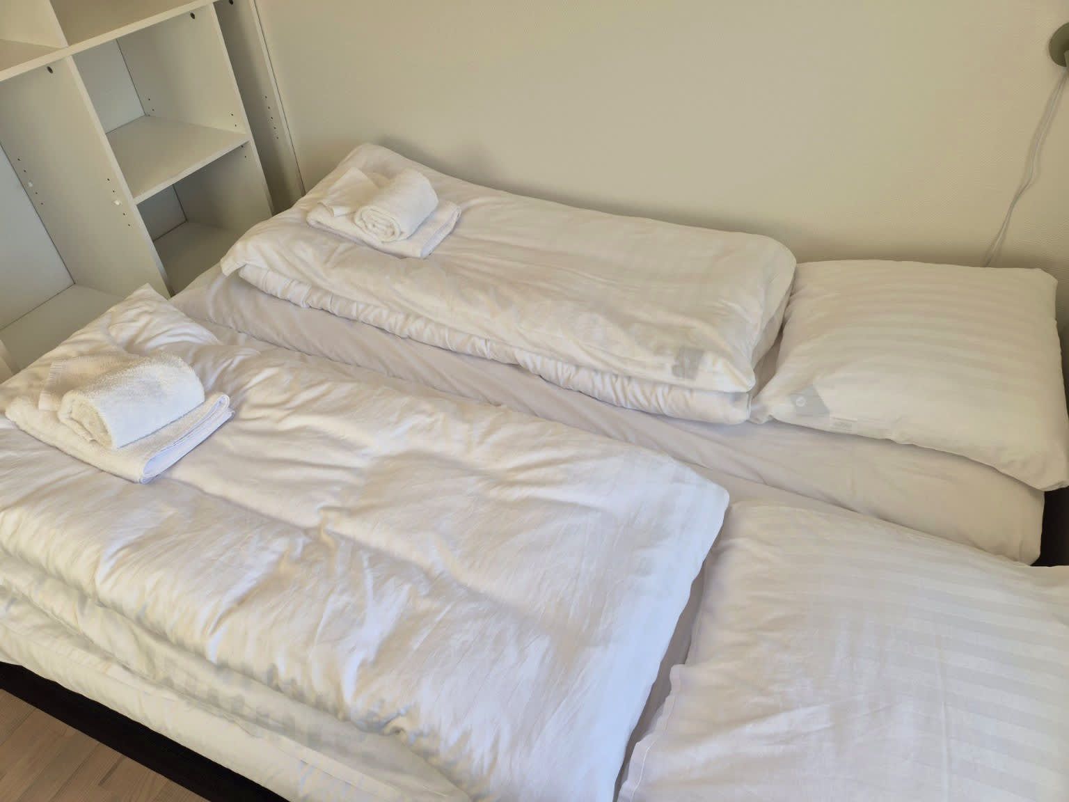 Et hotelværelse med to enkeltsenge, hver med et sammenrullet hvidt håndklæde.