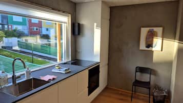 Et moderne køkken med indbygget ovn, vask og et vindue med udsigt over et boligområde.