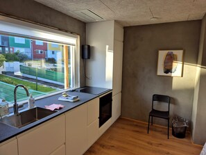 Et moderne køkken med indbygget ovn, vask og et vindue med udsigt over et boligområde.