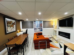 Uma sala de estar moderna com área de jantar, sofá, televisão e obras de arte nas paredes.