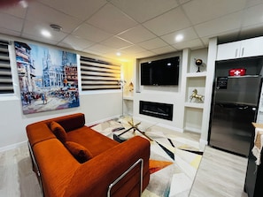 Ein modernes Wohnzimmer mit einer Couch, einem Flachbildfernseher, einem Kühlschrank und einem Bild an der Wand.