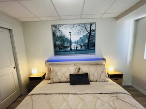 Ein Schlafzimmer mit einem Bett, einem Kopfteil, zwei Nachttischen und einem an der Wand hängenden Bild.