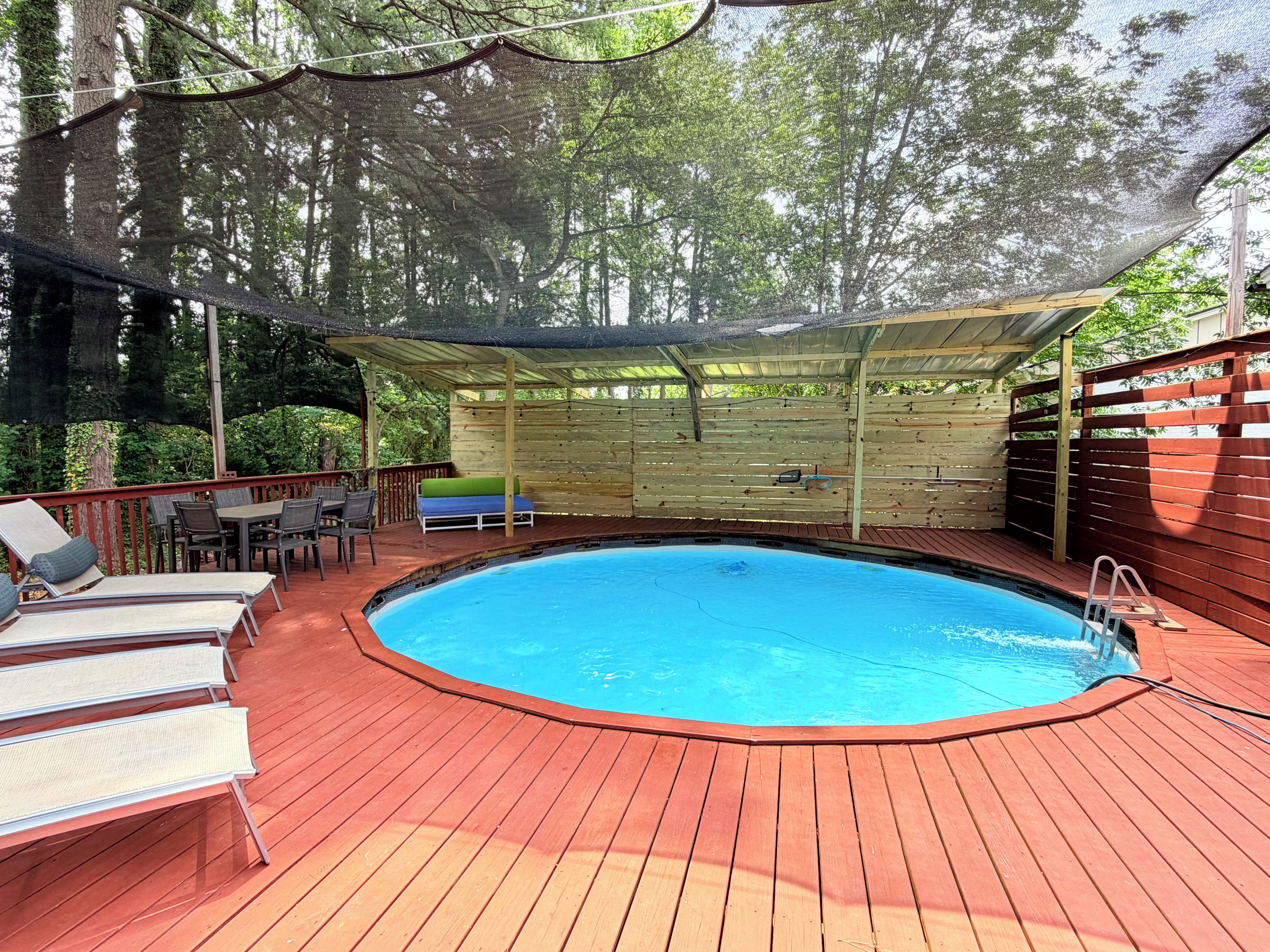 Une terrasse en bois avec une piscine, des chaises longues et un espace salon abrité.