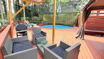Une terrasse extérieure couverte, aménagée avec des meubles en osier, une piscine et un barbecue.