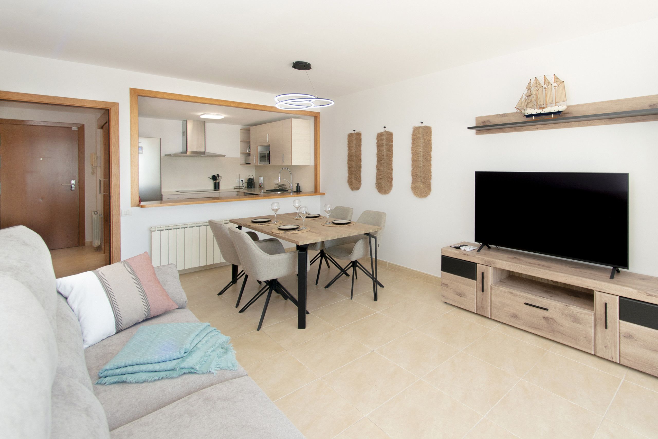 A modern living room with a dining area, a flat-screen TV, and a ship model on the wall.