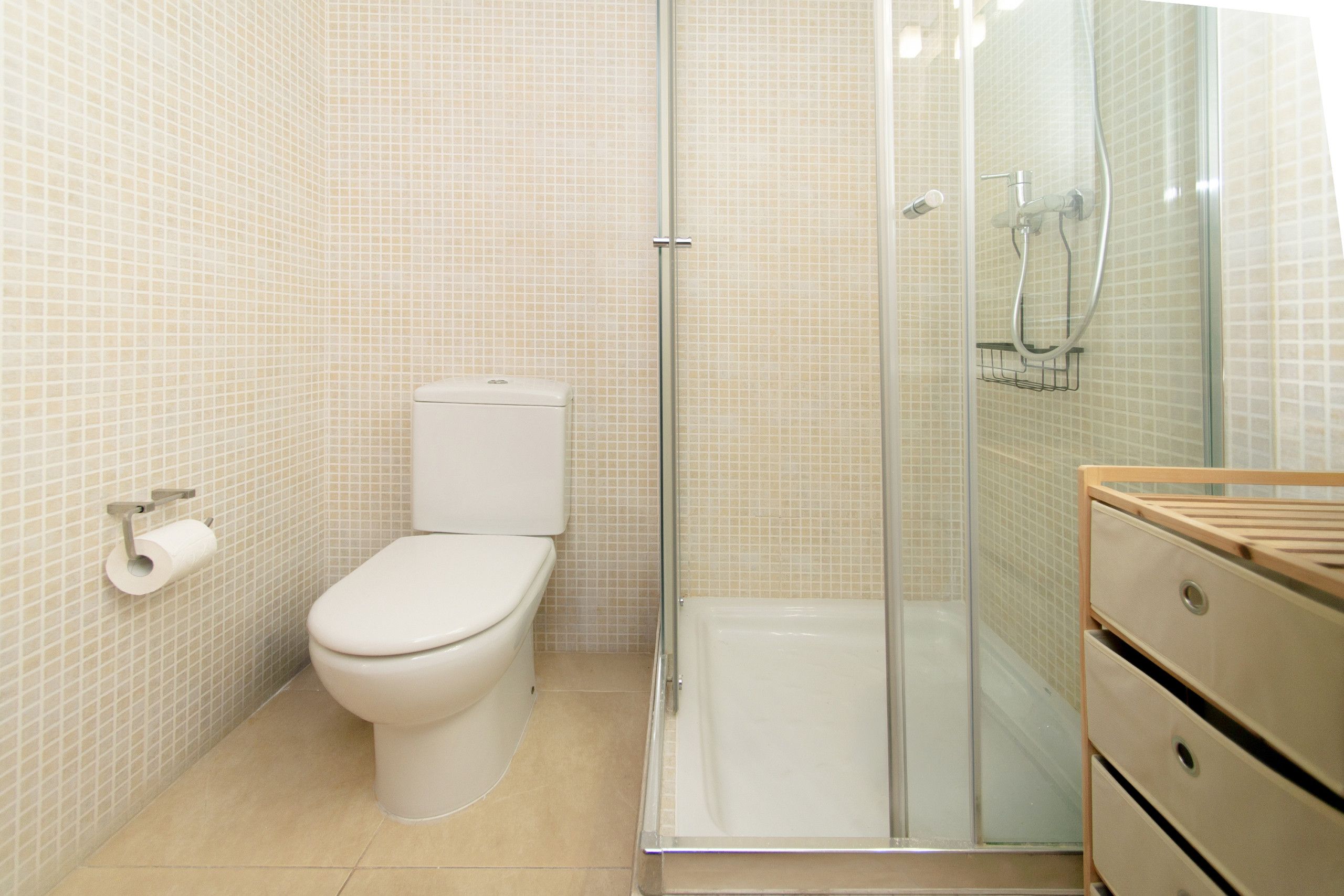 Un bagno con un water, box doccia in vetro e mobiletto in legno.