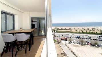 Un balcon avec une table et des chaises pour prendre les repas, une vue sur la plage et un espace de stationnement.