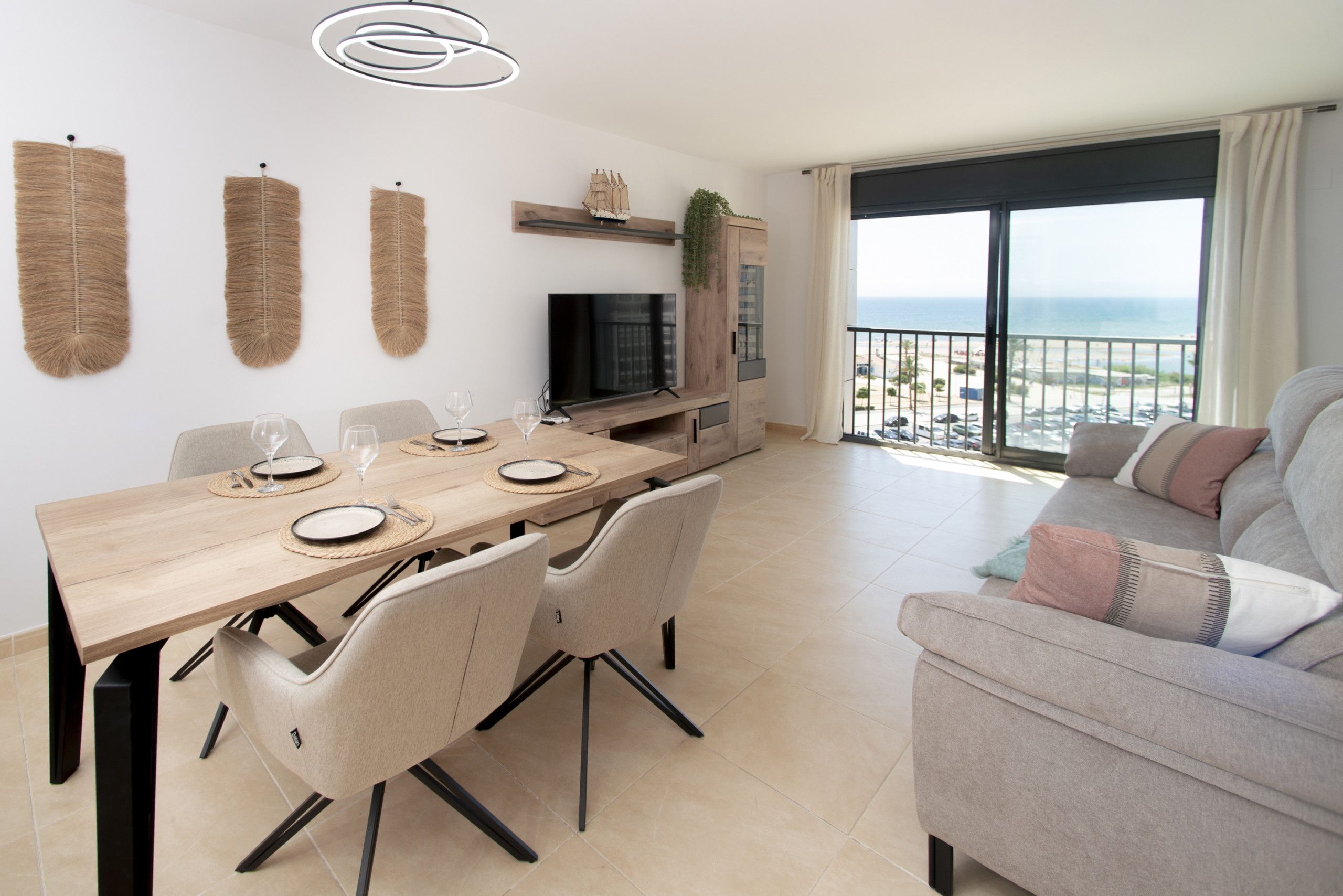 Una sala de estar moderna con comedor, televisor y balcón con vista al mar.