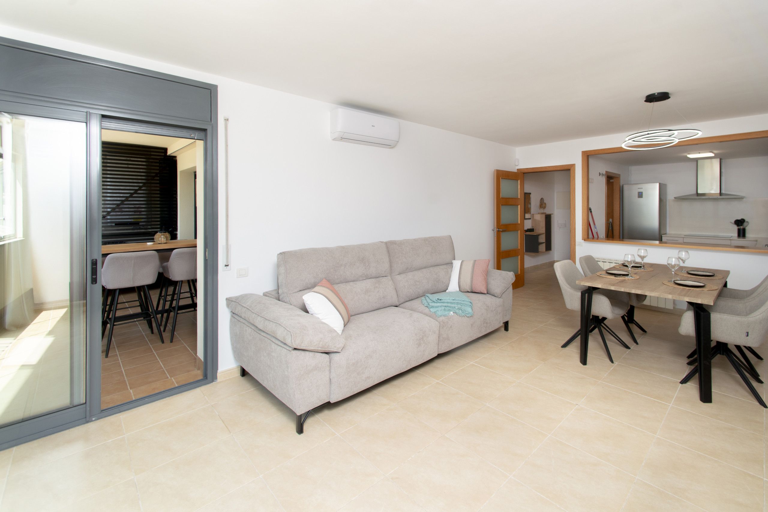 A modern living room with a sofa, a dining table with chairs, and a kitchen area visible through an open door.