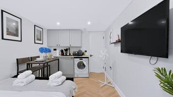 A modern hotel room with a bed, a dining area, a kitchen, a washing machine, and a TV.