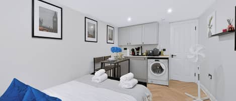 Una habitación de hotel con una cama, una almohada azul, una lavadora, un ventilador y cuadros en la pared.