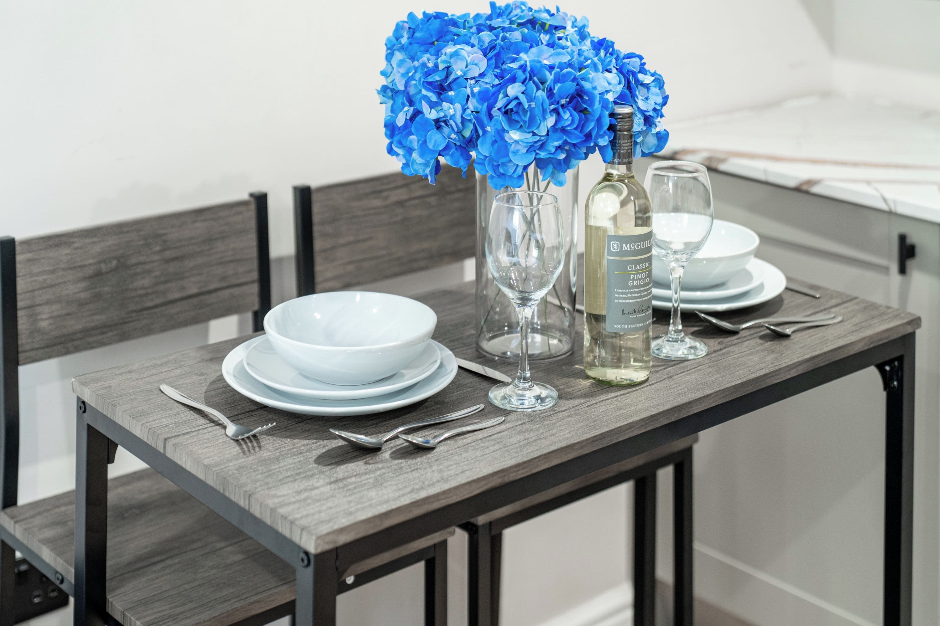 Une table à manger dressée avec de l’assiette blanche, une bouteille de vin et un verre.