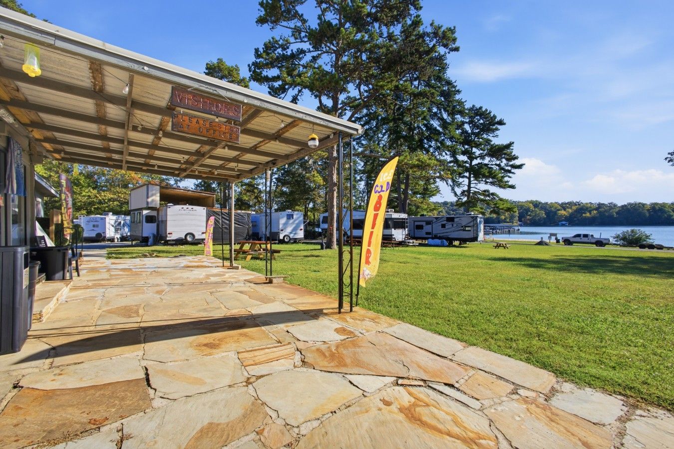 A covered outdoor area with a stone floor, a sign for a visitor's office, and RVs in the background.
