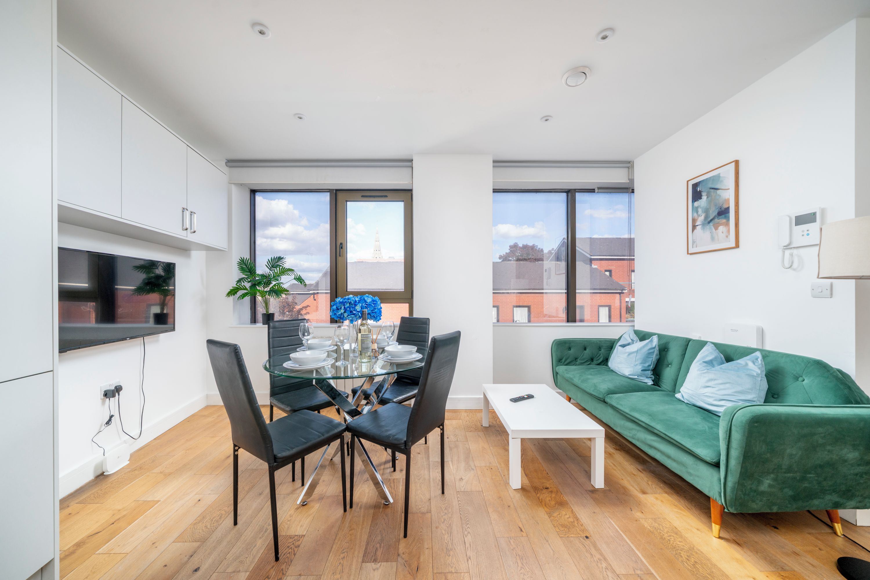 A modern apartment with a dining area, a green sofa, and a view of a building across the street.