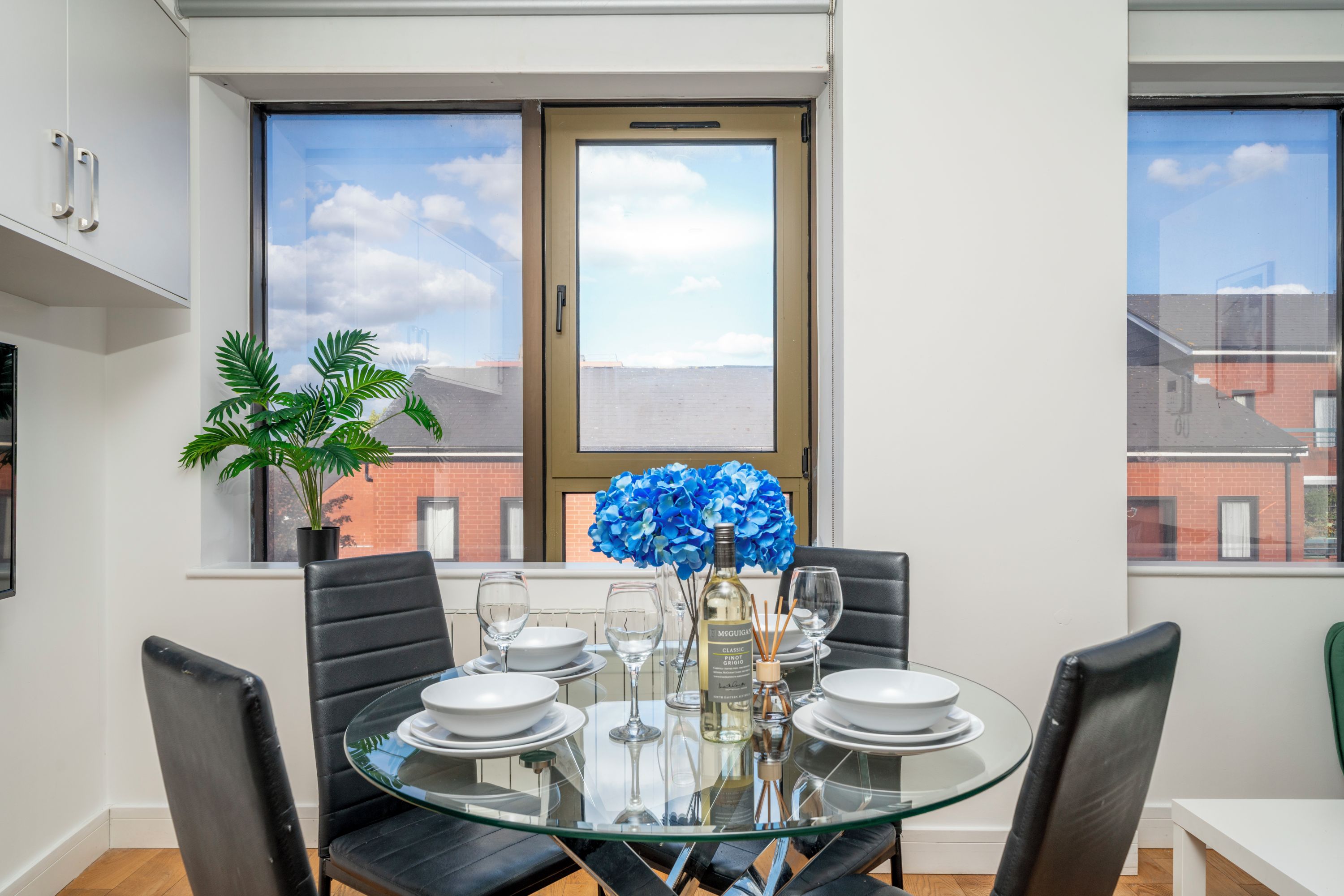 A dining area with a glass table, four chairs, and a potted plant.