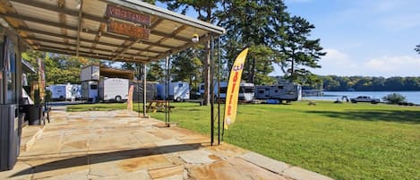 A covered outdoor area with a stone floor, a sign for a visitor's office, and RVs in the background.
