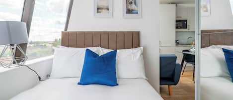 A modern hotel room with a large bed, a desk, and a view of the city.