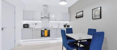 A modern kitchen with white cabinets, a dining table with blue chairs, and a pendant light.