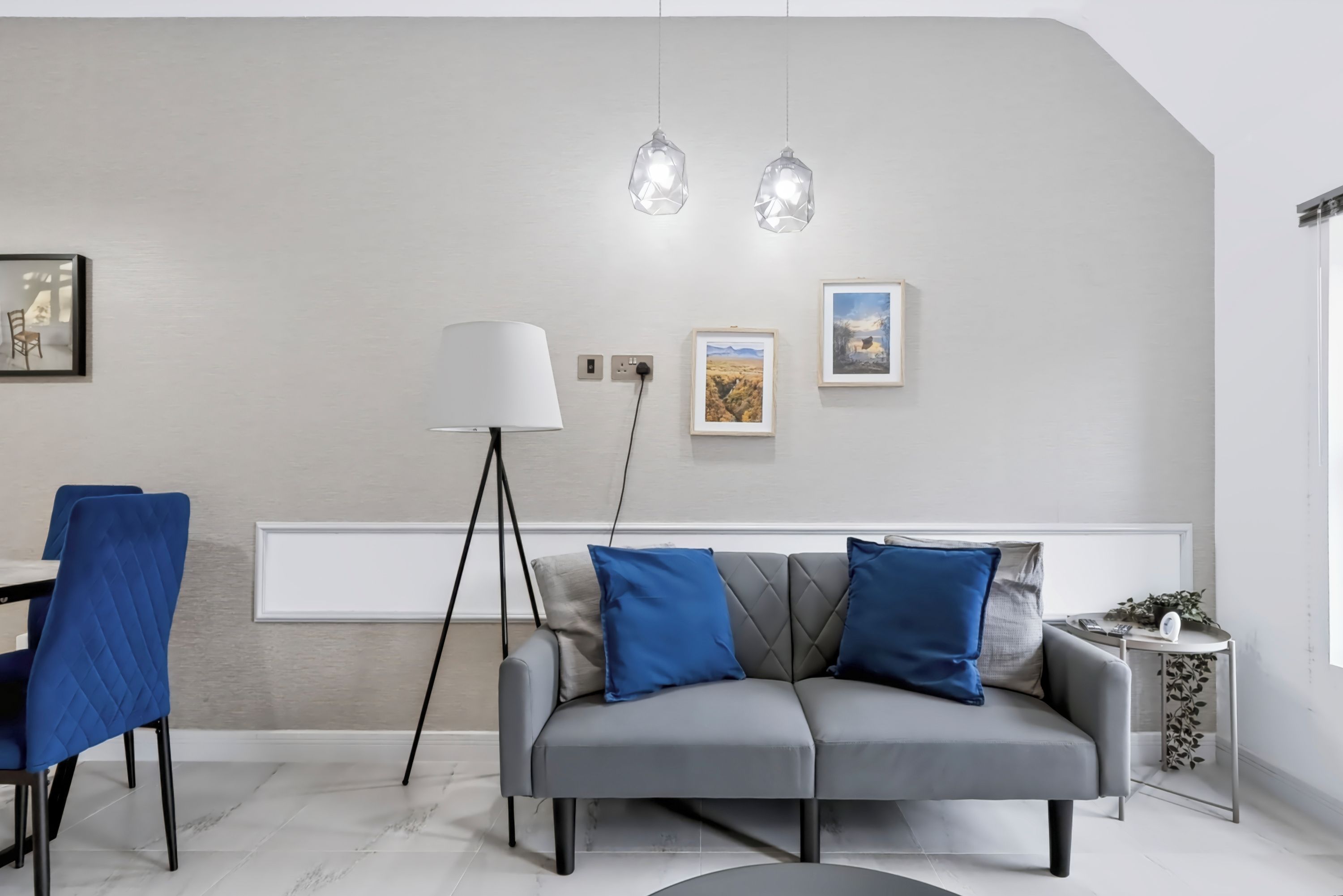 Un soggiorno moderno con un divano grigio, cuscini azzurri, una lampada da terra e due lampade a sospensione.