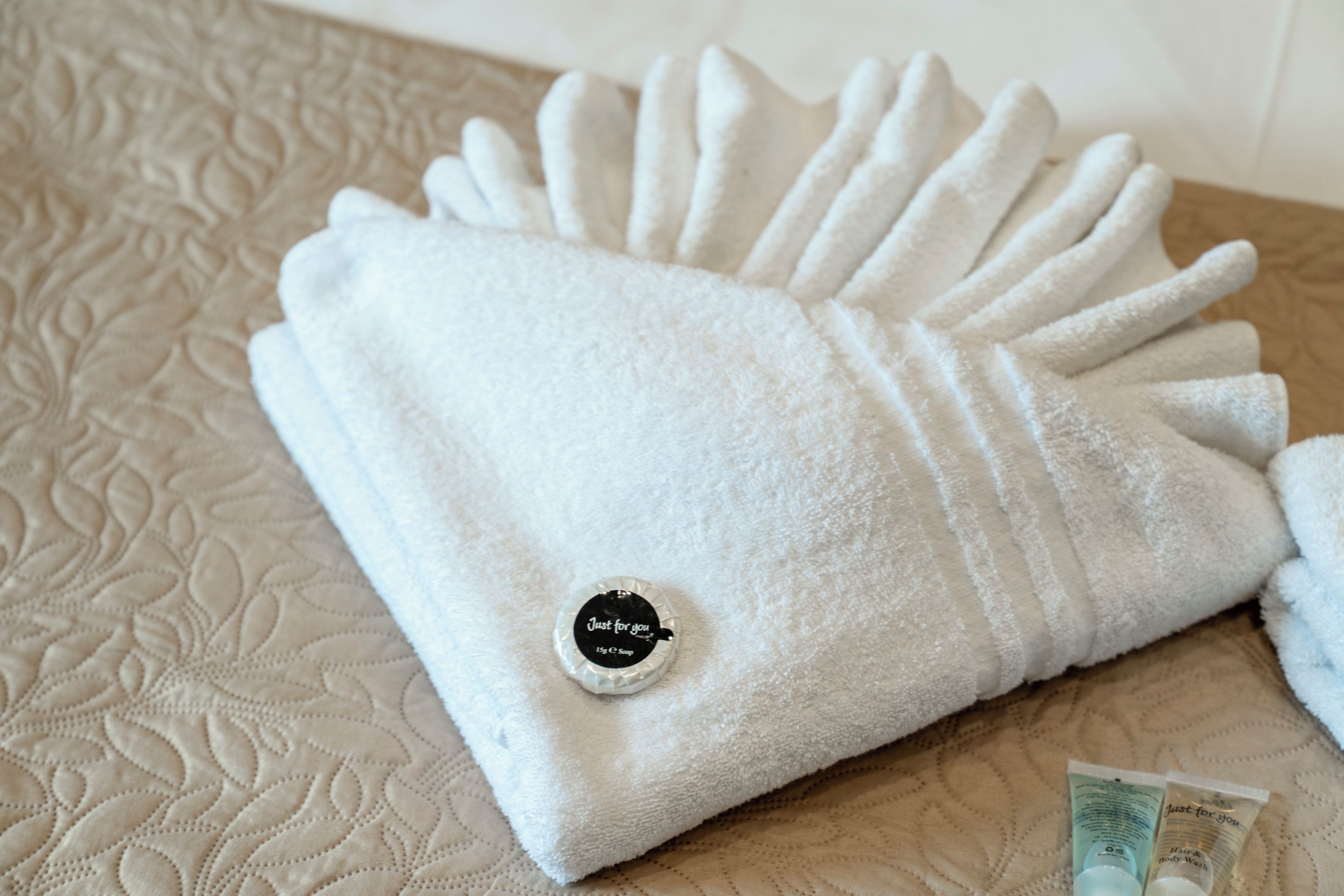 A neatly folded white towel with a black label on a textured beige bedspread.