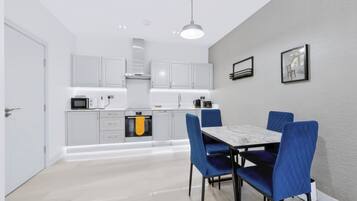 Una cocina moderna con armarios blancos, una mesa de comedor con sillas azules y una lámpara colgante.