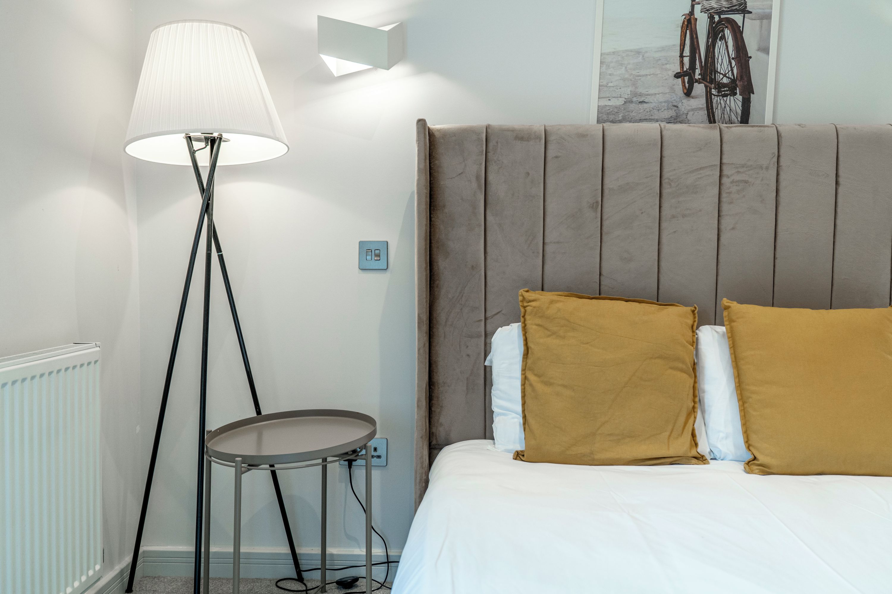 Ein Schlafzimmer mit einem Bett, einem Nachttisch, einer Stehlampe und einer Wandleuchte.