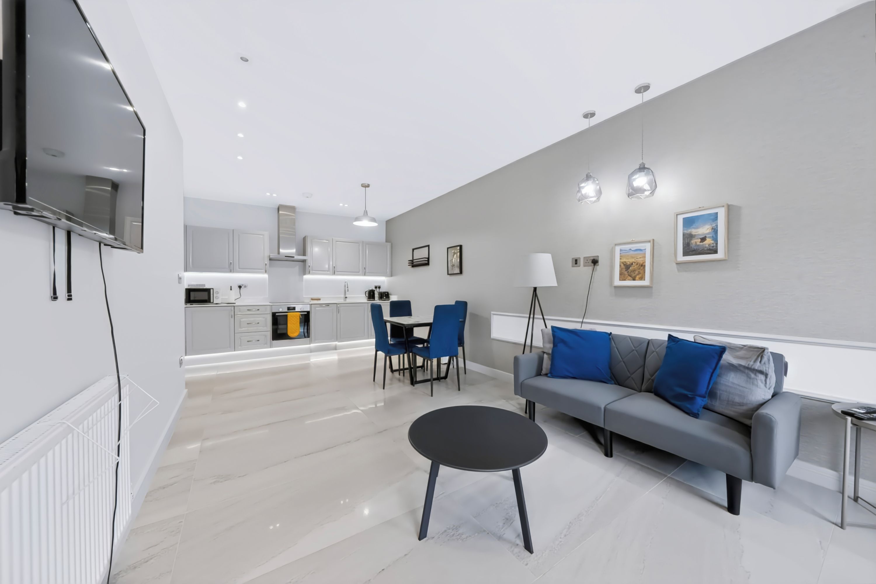 Un salon moderne avec un canapé gris, une table basse noire et un coin repas avec des chaises bleues.