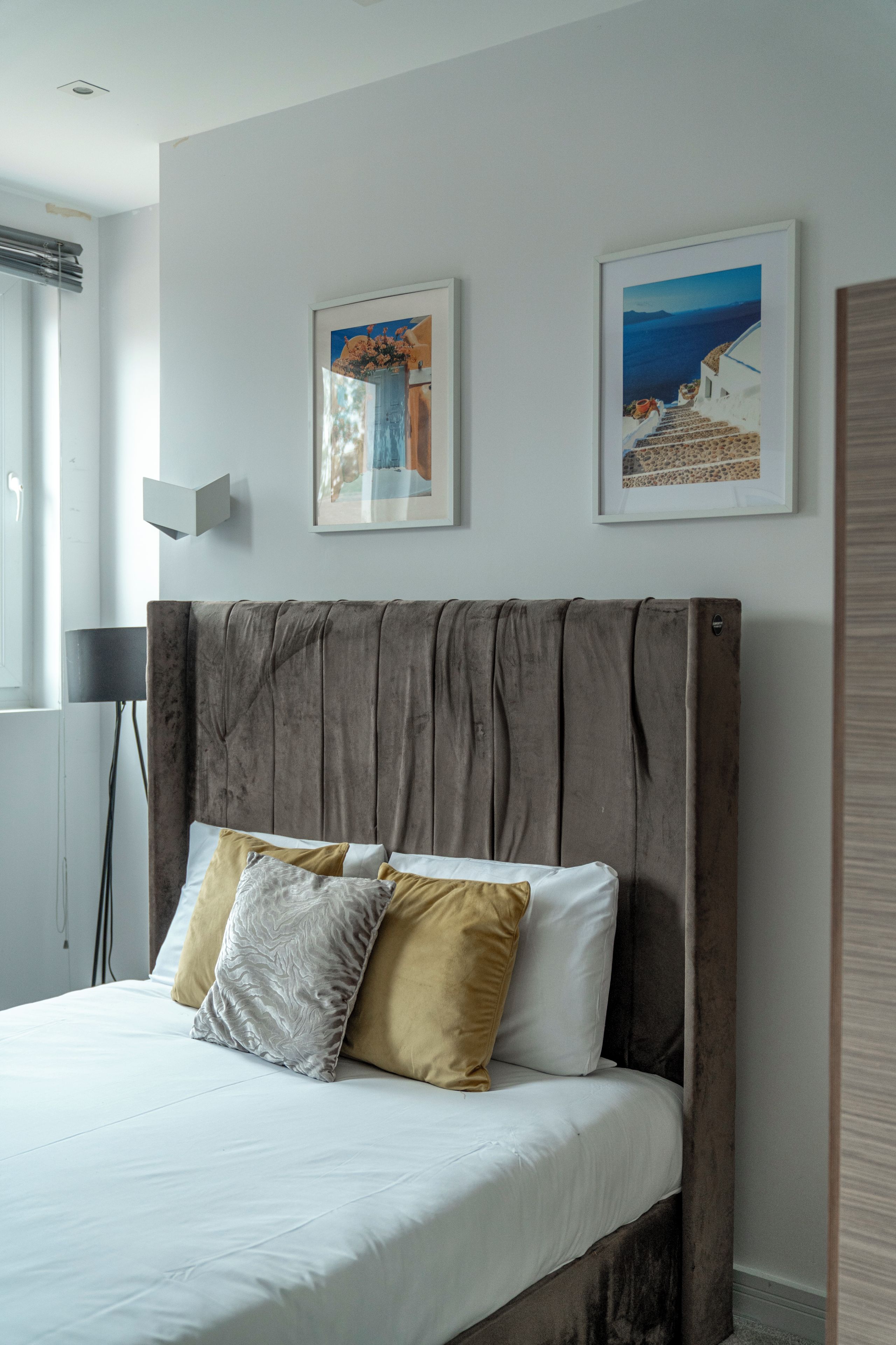 A bed with white bedding and two pillows, a wooden headboard, and two framed pictures on the wall.