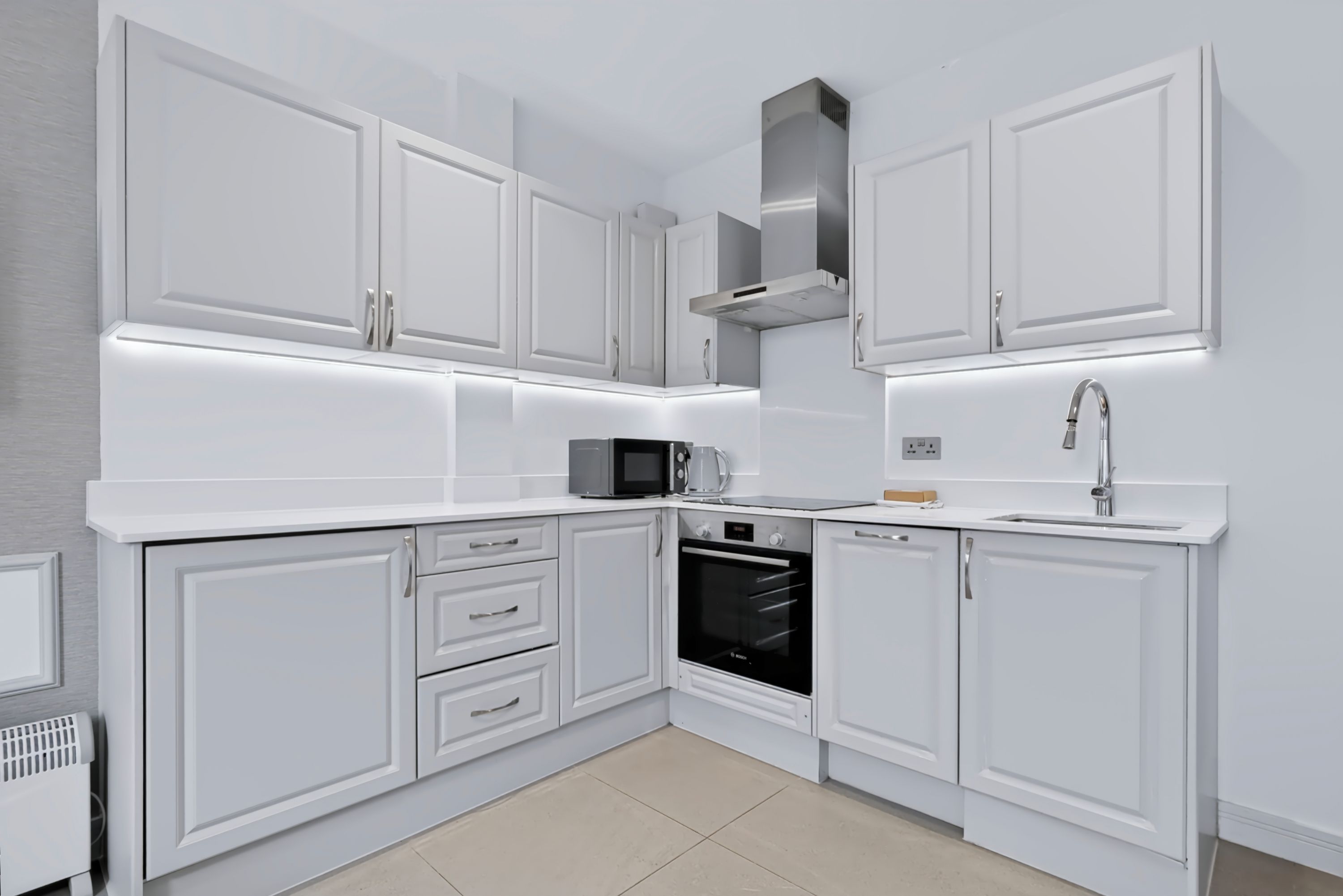 A modern kitchen with white cabinetry, a built-in oven, a microwave, and a stainless steel range hood.