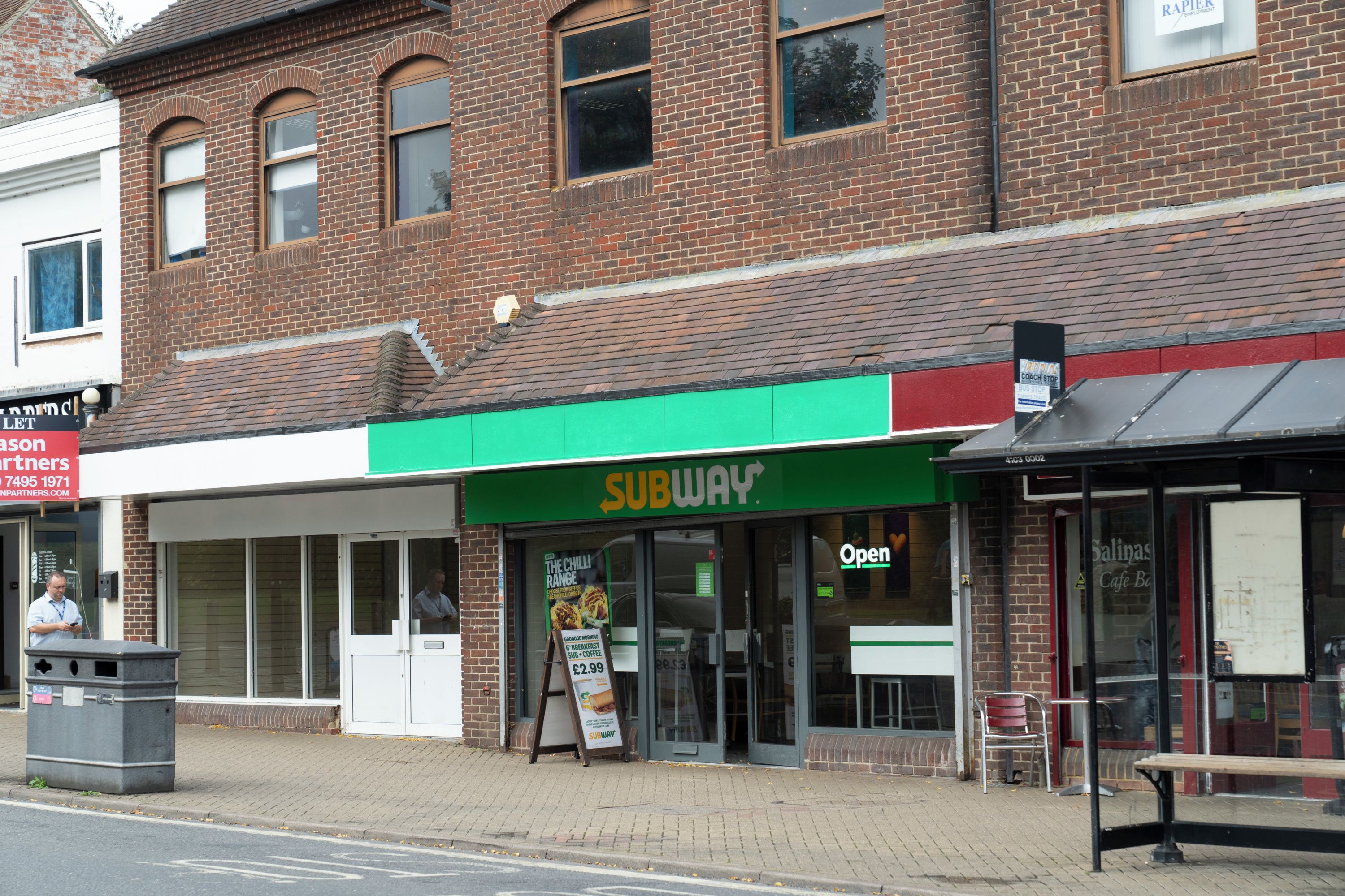 A Subway restaurant with a green awning and a sign indicating it's open.
