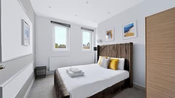 A modern bedroom with a large bed, a radiator, and two windows.