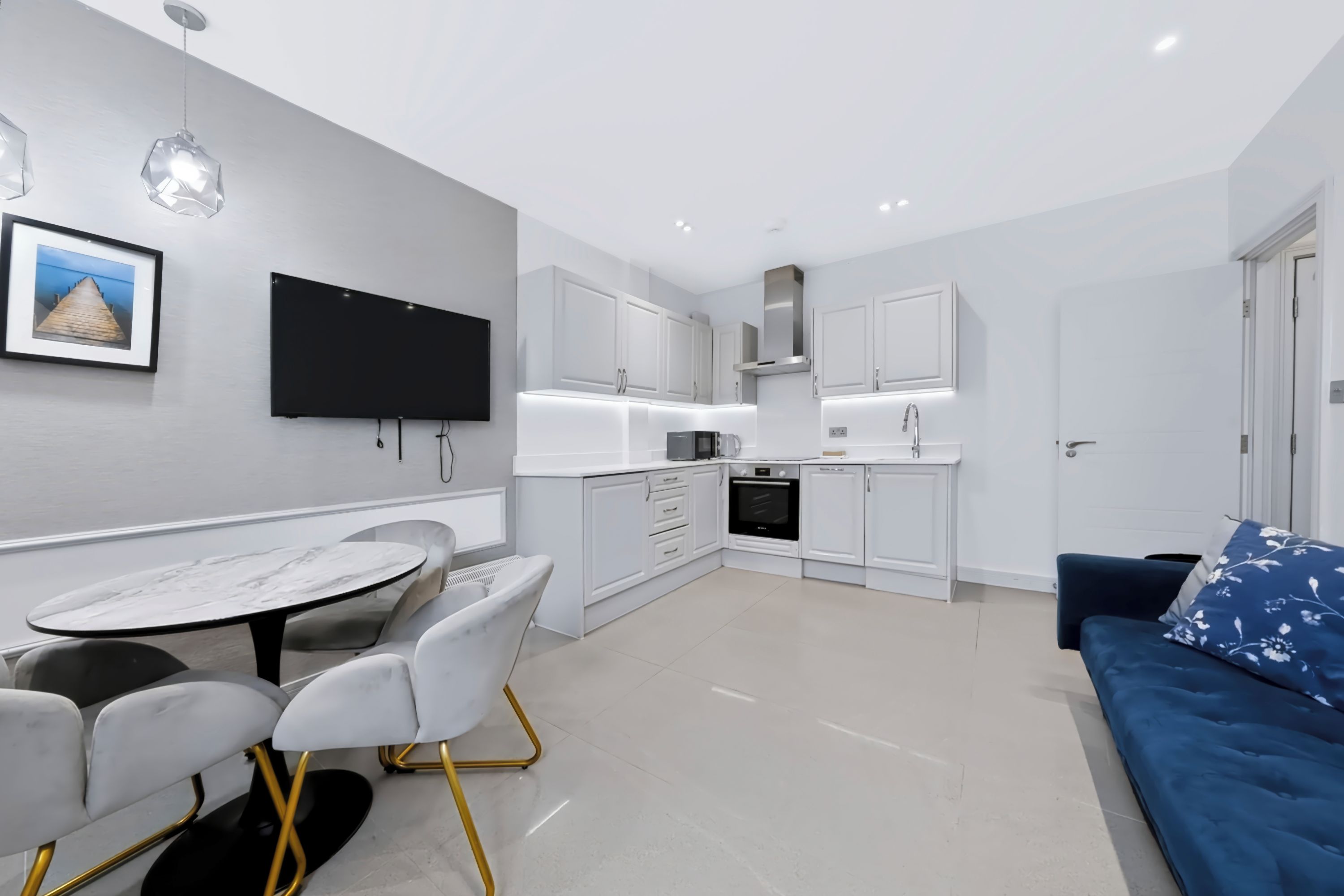 A modern kitchen with white cabinets, a built-in oven, and a dining area with a marble table and chairs.