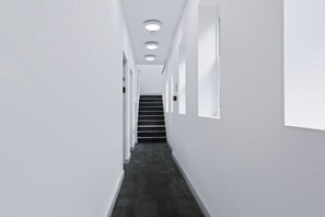 Ein schmaler, weiß getünchter Flur mit dunklem Boden, der zu einer Treppe führt.