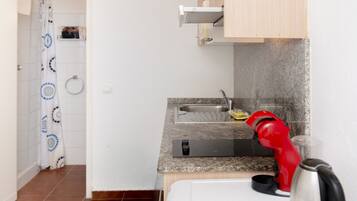 Een kleine keuken met een spoelbak, een kookplaat en een rode waterkoker.