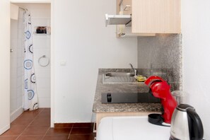 Een kleine keuken met een spoelbak, een kookplaat en een rode waterkoker.