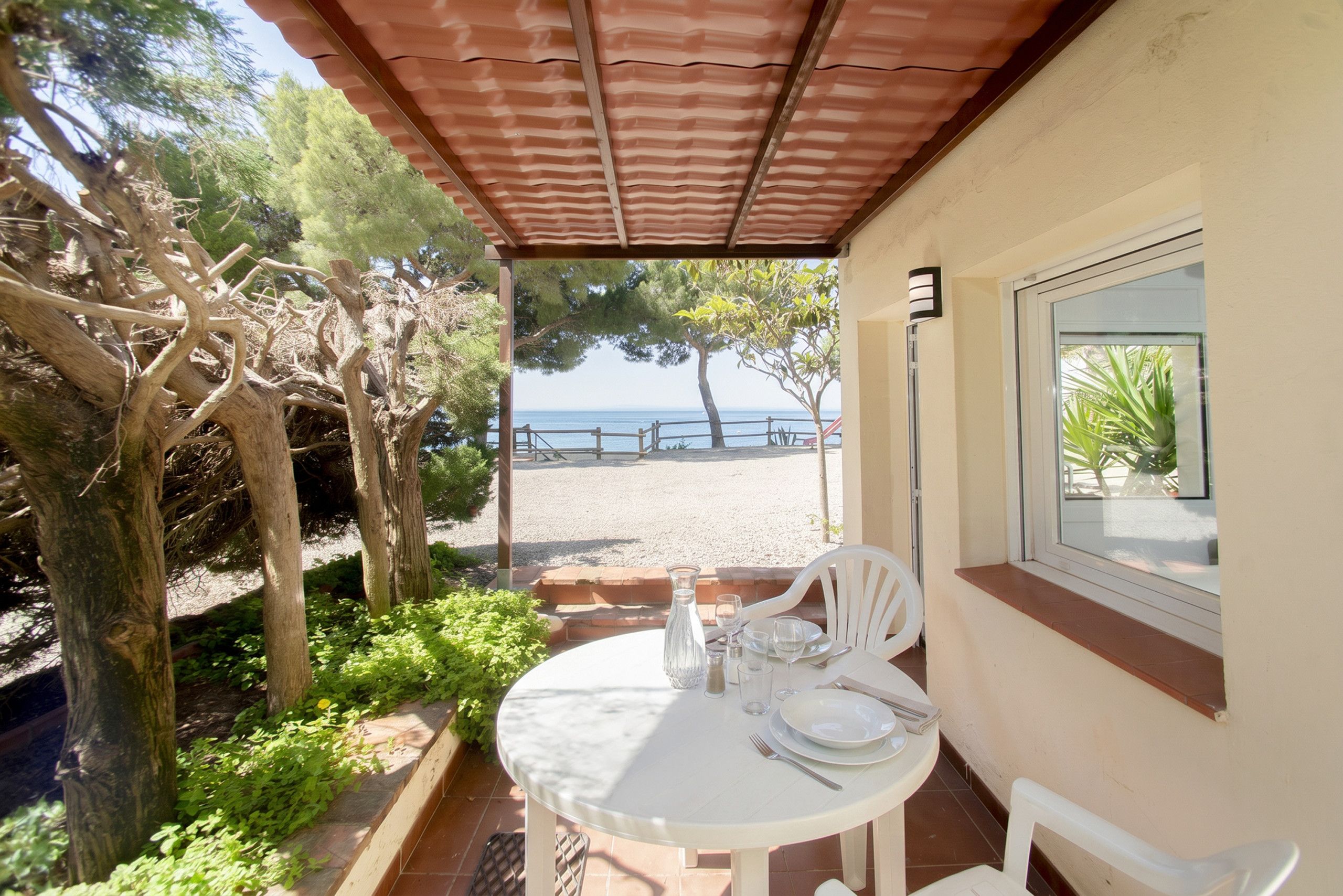 Un espacio de estar techado al aire libre con una mesa dispuesta para dos, con vista a una playa.